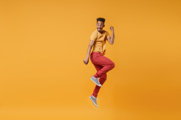 Fototapeta na wymiar Excited funny young african american guy in casual clothes posing isolated on yellow orange wall background studio portrait. People lifestyle concept. Mock up copy space. Jumping doing winner gesture.