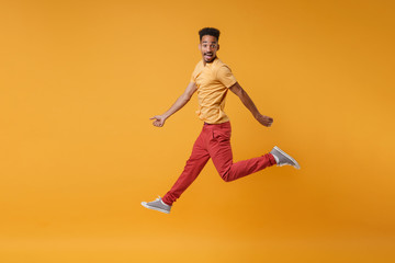 Fototapeta na wymiar Side view of excited young african american guy in casual clothes posing isolated on yellow orange background, studio portrait. People lifestyle concept. Mock up copy space. Jumping, looking camera.