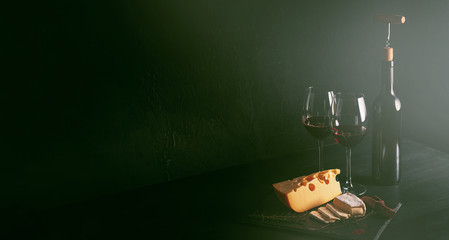 cheese and wine on the table. two glasses of red wine next to cheese. black wooden table. place for text. concept of a romantic dinner for two