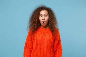 Smiling young african american girl in casual orange knitted clothes isolated on pastel blue background studio portrait. People sincere emotions, lifestyle concept. Mock up copy space. Looking camera.