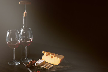 cheese and wine on the table. two glasses of red wine next to cheese. black wooden table. place for text. concept of a romantic dinner for two