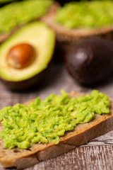 Avocado sandwiches next to cutted ones on wooden board