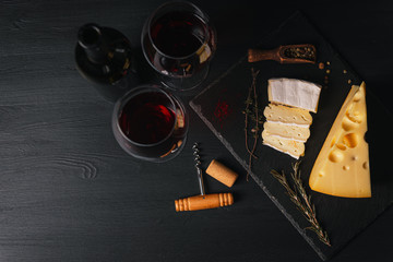 cheese and wine on the table. two glasses of red wine next to cheese. black wooden table. place for...
