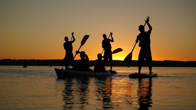 Paddle boarders silhouette of young sportsmen paddling on stand up board. Healthy lifestyle. Water sports. River sunset.