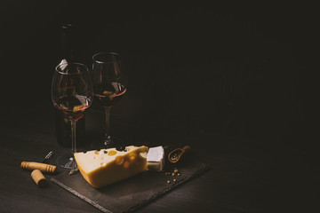 cheese and wine on the table. two glasses of red wine next to cheese. black wooden table. place for text. concept of a romantic dinner for two