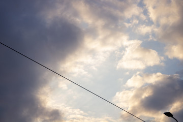 A lantern pole against the background of a cloud sky with sunsets; In the background, industrial buildings and houses overlooking the park