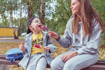 Happy cheerful Young family, little boy 3-5 years old, mother woman, Eat pink ice cream on a stick. Summer in city, autumn day. Casual clothes, jeans. Emotions of joy weekend fun and relaxation.
