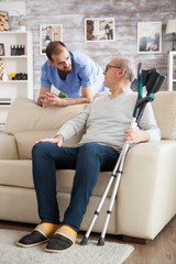 Senior man sitting on couch with crutches in nursing home