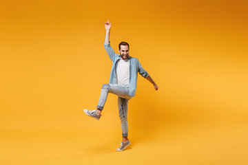 Cheerful young bearded man in casual blue shirt posing isolated on yellow orange background studio portrait. People emotions lifestyle concept. Mock up copy space. Jumping, pointing index finger up.