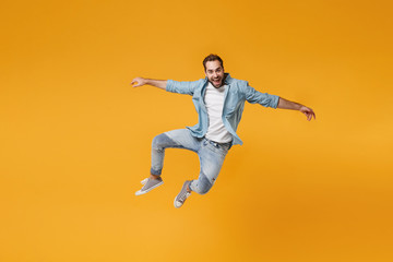 Obraz na płótnie Canvas Cheerful young bearded man in casual blue shirt posing isolated on yellow orange background, studio portrait. People sincere emotions lifestyle concept. Mock up copy space. Jumping spreading hands.