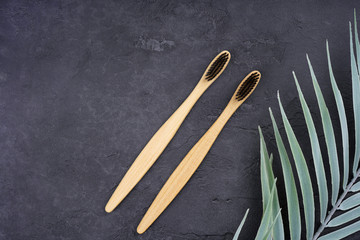 Two bamboo toothbrushes, palm leaf decor on gray concrete background. Love, healthcare, zero waste,...