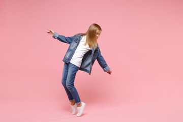 Little blonde kid girl 12-13 years old in denim jacket isolated on pastel pink wall background children studio portrait. Childhood lifestyle concept. Mock up copy space. Standing on toes, dancing.