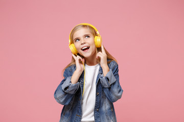 Charming little kid girl 12-13 years old in denim jacket isolated on pastel pink background children studio portrait. Childhood lifestyle concept. Mock up copy space. Listen music with headphones.