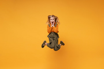 Fototapeta na wymiar Shocked little kid girl 12-13 years old in turtleneck, jumpsuit isolated on orange yellow background in studio. Childhood lifestyle concept. Mock up copy space. Jumping, screaming, put hands on cheek.