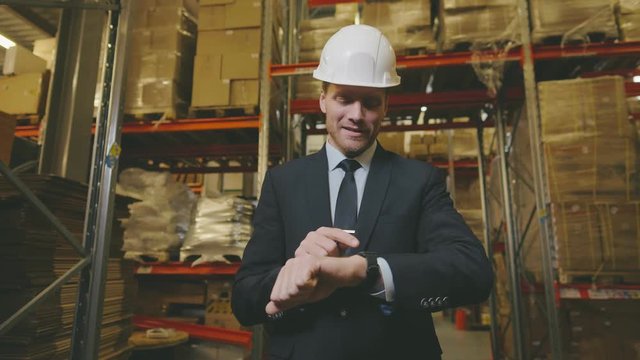 Entrepreneur using app on smartwatch standing against high shelves in modern warehouse