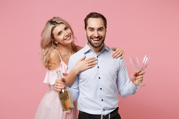 Cheerful young couple two guy girl in party outfit celebrating posing isolated on pastel pink background. Valentine's Day Women's Day birthday holiday party concept. Holding glass bottle of champagne.