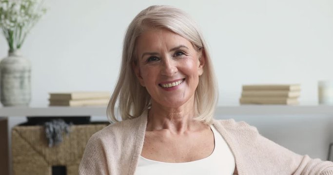 Happy older middle aged woman looking at camera at home