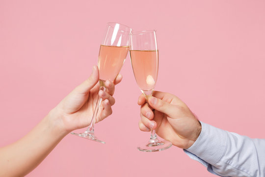 Close up cropped photo of female, male hold in hands glass of champagne isolated on pastel pink background. Copy space advertising mock up. Valentine's Day Women's Day birthday holiday party concept.