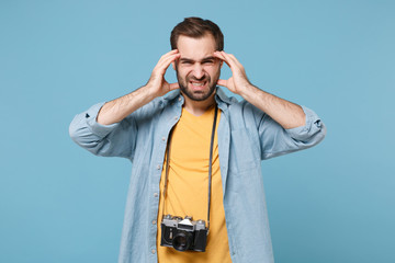 Sick traveler tourist man in yellow clothes with photo camera isolated on blue background. Male passenger traveling abroad on weekends. Air flight journey concept. Put hands on head, having headache.