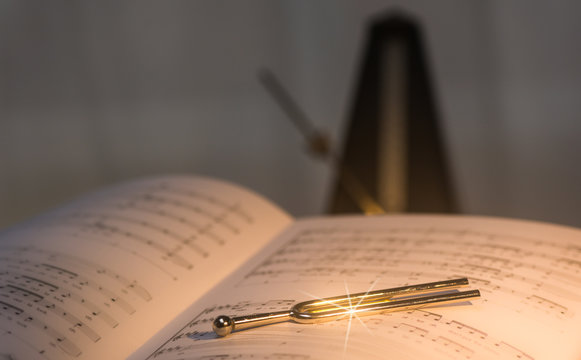 Stimmgabel liegt auf alten, historischen Noten. Im Hintergund, in der Unsch&auml;rfe steht ein Metronom. Selektive Sch&auml;rfe