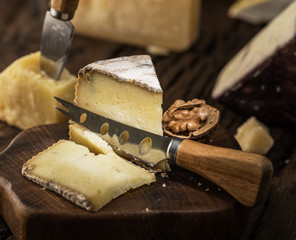 Piece of homemade goat cheese and cheese knife on the wooden board. Cheese background.