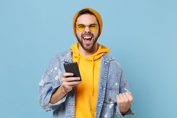 Joyful hipster guy in fashion jeans denim clothes posing isolated on pastel blue background. People...