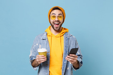 Surprised young hipster guy in fashion jeans denim clothes posing isolated on pastel blue...