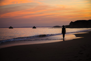 Fototapeta na wymiar Portugal, Algarve, The best beaches of Portimao, Praia da Rocha, lilac golden sunset over the waves of The Atlantic Ocean, a girl walking the waves, silhouette happy woman at sunset on the beach