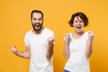 Joyful young couple friends bearded guy girl in white empty blank t-shirts posing isolated on yellow orange background. People lifestyle concept. Mock up copy space. Doing winner gesture, screaming.