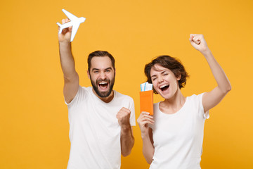 Joyful young couple friends bearded guy girl in white t-shirts isolated on yellow orange background. People lifestyle concept. Mock up copy space. Hold passport ticket air plane doing winner gesture.