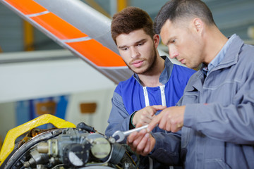 two mechanics working on a small aircraft in a hangar