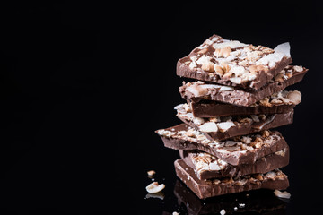 Stack of Broken Chocolate Pieces on Black Background. Copy Space. Closeup View