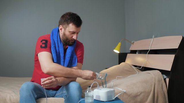 Man screws inhalation mask to nebulizer. Young man sits alone in room and fastens mask to inhaler. Slow motion and general plan