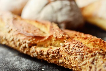 Bakery products. Crispy, beautiful bread on a dark background. Buckwheat, without yeast, wheat bread with flax and sunflower seeds. Top view, place for text.Tasty baguette. Close up