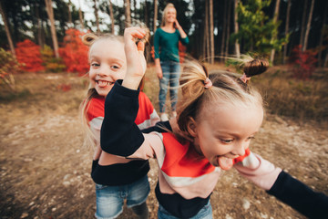 Blonde mother and her twin daughters are walking in the autumn forest among red trees.