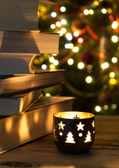 beautiful candle on a wooden table with a stack of books and christmas garlands on the background