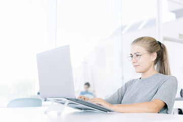 Profile of a blonde girl working with a laptop in a coworking and people around