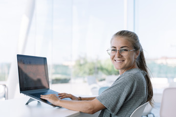 Blonde girl with glasses turned to face the camera while working in front of a laptop