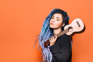 portrait of hipster woman with violet dreadlocks and ukulele in her hands on an orange background