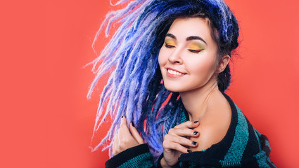 Portrait of a beautiful woman with violet dreadlocks and color make-up on a red background. Makeup...