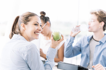 Girl holding an apple while she's smiling at a table with other people