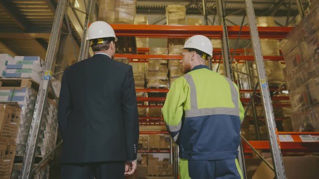 Entrepreneur and warehouse worker discussing terms of cargo delivery standing in warehouse