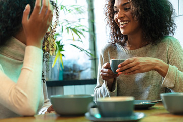 Two cheerful young african girlfriends sitting at the cafe