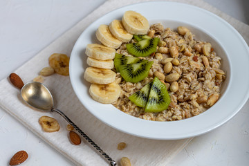 Breakfast consisting of oatmeal, nuts and fruits. Kiwi, banana, pomegranate and almonds decorate the plate. Healthy food, on a white background.