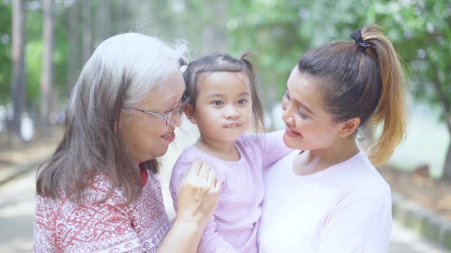 Slow motion of cute little girl kissed by her mother and grandmother at the park