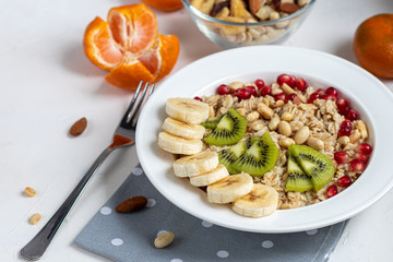 Breakfast consisting of oatmeal, nuts and fruits. Kiwi, banana, pomegranate and almonds decorate the plate. Healthy food, on a white background.