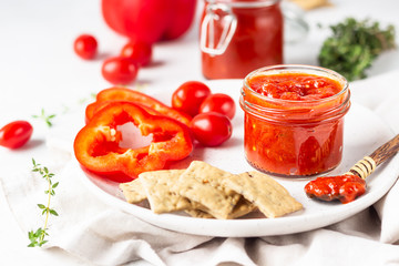 Ajvar (pepper mousse) or pindjur red vegetable spread made from paprika and tomatoes in glass jar on light stone table. Serbian native food.