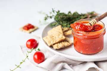 Ajvar (pepper mousse) or pindjur red vegetable spread made from paprika and tomatoes in glass jar on light stone table. Serbian native food.