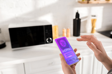cropped view of woman holding smartphone with shopping app