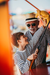 Fototapeta na wymiar Grandfather and grandson having fun and spending good quality time together in amusement park. Kid shooting with air gun while grandpa helps him to win the prize.